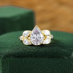 an engagement ring with three pear shaped diamonds on top of a green velvet cushion in front of a wooden floor