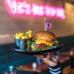 a person holding a plate with a hamburger and fries on it in front of a neon sign