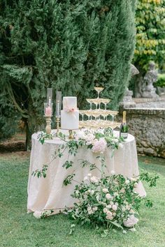 a table topped with cake and flowers on top of a lush green field next to trees