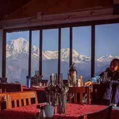 a man sitting at a table in front of a window looking out on the mountains