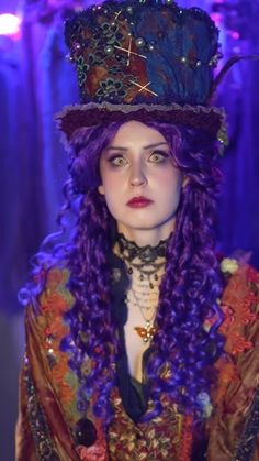 a woman with long purple hair wearing a hat and dress in front of blue lights