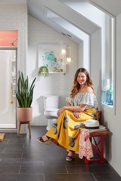 a woman sitting on top of a wooden bench next to a potted plant in a bathroom