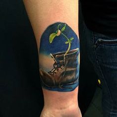 a tattoo on the arm of a person with a boot and plant growing out of it