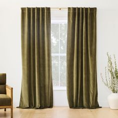 a living room with a chair and window covered in green velvet curtains next to a potted plant