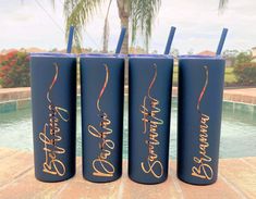 three blue tumbles with gold writing on them sitting next to a pool and palm tree