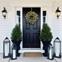 front door decorated with lanterns and wreaths for the holiday season, including two large potted trees