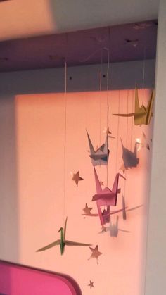 some origami cranes hanging from the ceiling in a room with pink walls and purple carpet