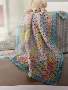 a crocheted blanket with a teddy bear sitting on top of it next to a window