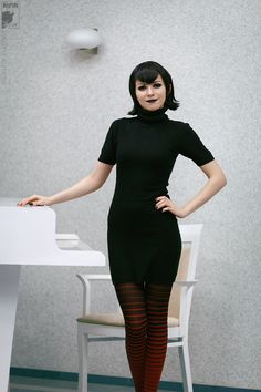 a woman standing in front of a table with a white chair next to it and wearing tight stockings