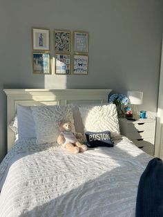 a white bed topped with pillows and a teddy bear sitting on it's side