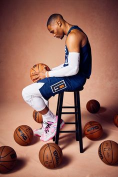 a man sitting on top of a stool next to basketballs in front of him