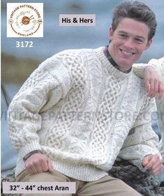 a man wearing a white sweater and tan pants sitting on a rock next to the ocean