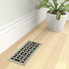 a potted plant sitting on top of a wooden floor next to a drain grate