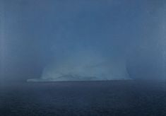 an iceberg floating in the middle of the ocean on a foggy day with blue skies