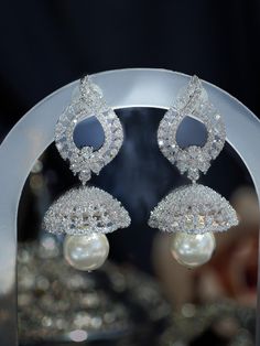 Our dainty Nova Jhumka is a contemporary pearl drop cubic zirconia earring. This artisinal South Asian inspired jewelry piece is adorned with white gold plating, cubic zirconia stones, and a lustrous pearl drop accent. The diamond-like sparkle of this CZ jhumka makes it the perfect accessory for a black-tie event or cultural occasion. Materials: Cubic zirconia, pearls, copper and brass alloy, rhodium plating Dimensions (L x W): 2.0 x 0.9 inches Weight: 9g (per jhumka) Luxury Heavy Round Jhumkas, Luxury Bollywood Style Pearl Drop Jhumkas, Luxury Heavy Temple Jewelry Jhumkas, Luxury Pearl Drop Chandbalis For Festive Occasions, Luxury Bollywood Chandelier Earrings For Celebration, Luxury Silver Bollywood Style Jhumkas, Luxury Temple Jewelry Bridal Earrings With American Diamond, Luxury Sterling Silver Chandbali Earrings, Luxury Temple Jewelry Chandelier Earrings For Festive Occasions