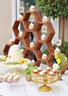 a table topped with cupcakes and cakes next to a wooden hexagonal stand