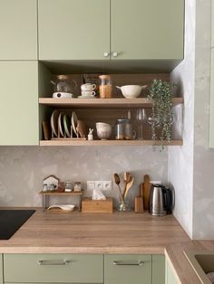 a kitchen with green cupboards and wooden counter tops in the center, filled with dishes and utensils