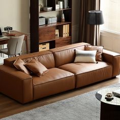 a brown leather couch sitting in front of a wooden book shelf next to a window