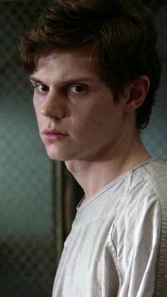 a young man in a white shirt looking at the camera with a serious look on his face