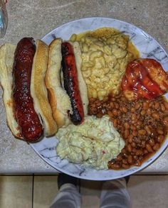 a plate full of food including beans, macaroni and cheese with hot dogs