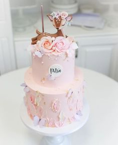 a pink cake decorated with flowers and a deer on top is sitting on a table