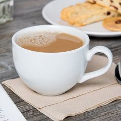 a cup of coffee sitting on top of a wooden table next to some pastries