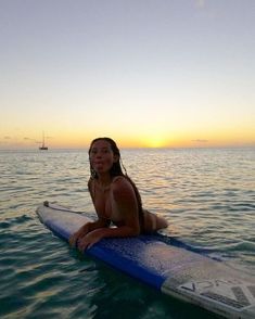 a woman sitting on top of a surfboard in the middle of the ocean at sunset