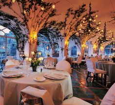 a dining room with tables and chairs covered in white linens is lit by candles