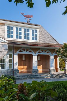 a house with two large wooden doors on the front and side of it, surrounded by greenery