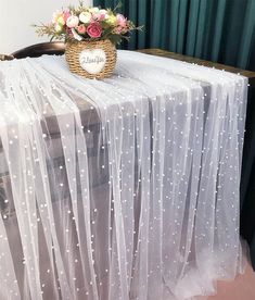 the table is covered with white sheer fabric and has flowers on it, along with a heart - shaped sign that says love