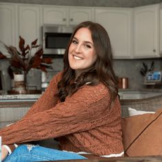 a woman is sitting on a couch in the kitchen with her arms crossed and looking at the camera