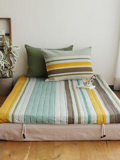 a bed with two pillows on top of it next to a potted plant and window