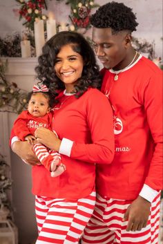 a man and woman in matching red pajamas holding a small child wearing striped pyjamass