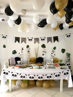 a party table with panda decorations and balloons on the ceiling is decorated in black, white and gold