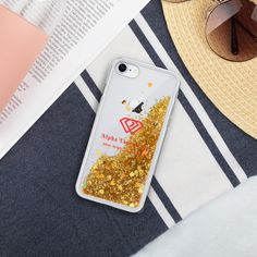 an iphone case with gold glitter on it sitting next to sunglasses and a straw hat