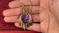 This vintage 14K yellow gold pendant is suspended from an 18K yellow gold chain finished with a 14K yellow gold spring ring clasp. The pendant is centered with one (1) heart mixed cut natural amethyst set into a three-prong setting. The center stone is bordered to each side by three (3), prong set, round mixed cut natural rubies. The pendant measures 56.7mm X 33.2mm. The serpentine style neck chain measuring 24 inches in length. The pendant necklace shows a soft patina. Ruby Pendant Necklace, Ruby Necklace Pendant, Amethyst Set, Ruby Pendant, Neck Chain, Yellow Gold Chain, Vintage Heart, Yellow Gold Pendants, Natural Ruby