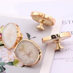 two gold cufflinks with white and black designs on them sitting next to a flower