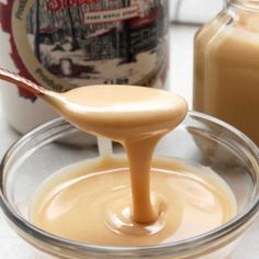 a spoon full of caramel sauce sitting on top of a glass bowl filled with liquid