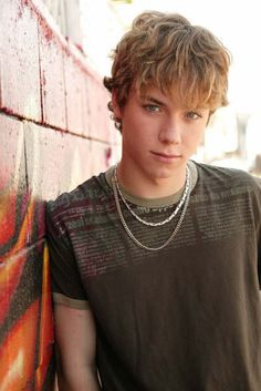 a young man standing in front of a graffiti covered wall