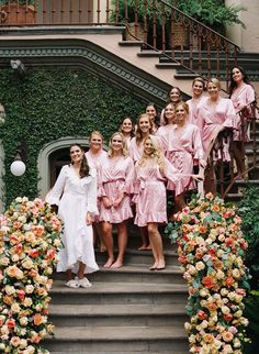 a group of women in pink robes standing on the steps of a building with flowers