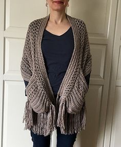 a woman standing in front of a white wall wearing a gray knitted shawl