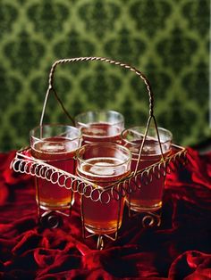 four glasses and a basket on a red cloth with green wallpaper in the background