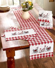 a wooden table topped with red and white checkered placemats next to a vase filled with flowers