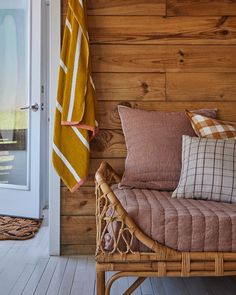 a wicker bench with pillows on it in front of a wood paneled wall