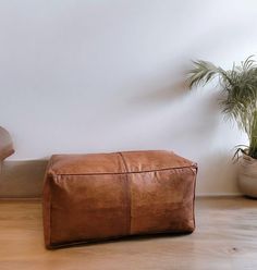 a brown leather ottoman sitting on top of a hard wood floor next to a potted plant