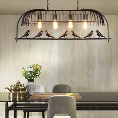 a dining room table and chairs with birds on the light fixture above it, along with two vases filled with flowers