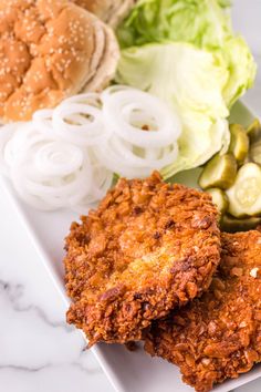 two fried chicken patties on a white plate with lettuce, cucumbers and pickles