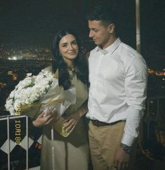 a man and woman standing next to each other with flowers in their hands at night