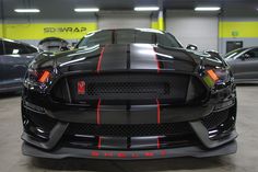 the front end of a black sports car in a garage with other cars behind it