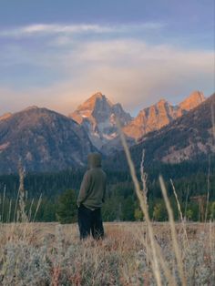 a man standing in the middle of a field with mountains in the background at sunset